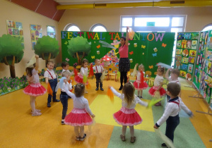 Dzieci tańczą w kole, w rękach trzymają chusteczki, które unoszą na przemian w górę.